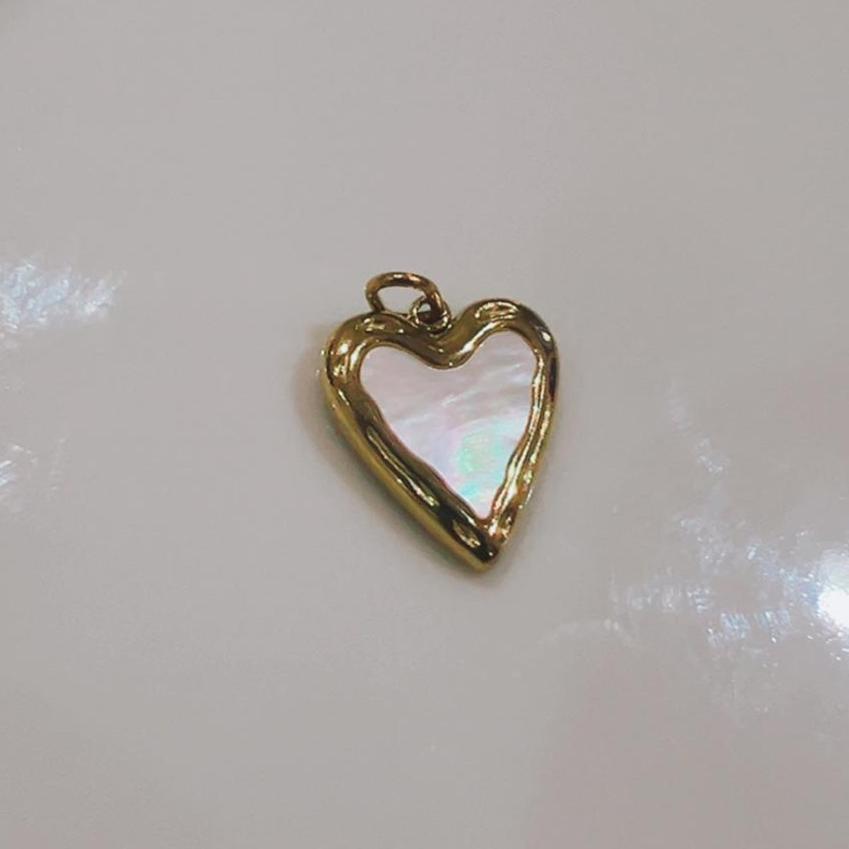 Pearly white heart charm with a gold-coloured edge on a white background