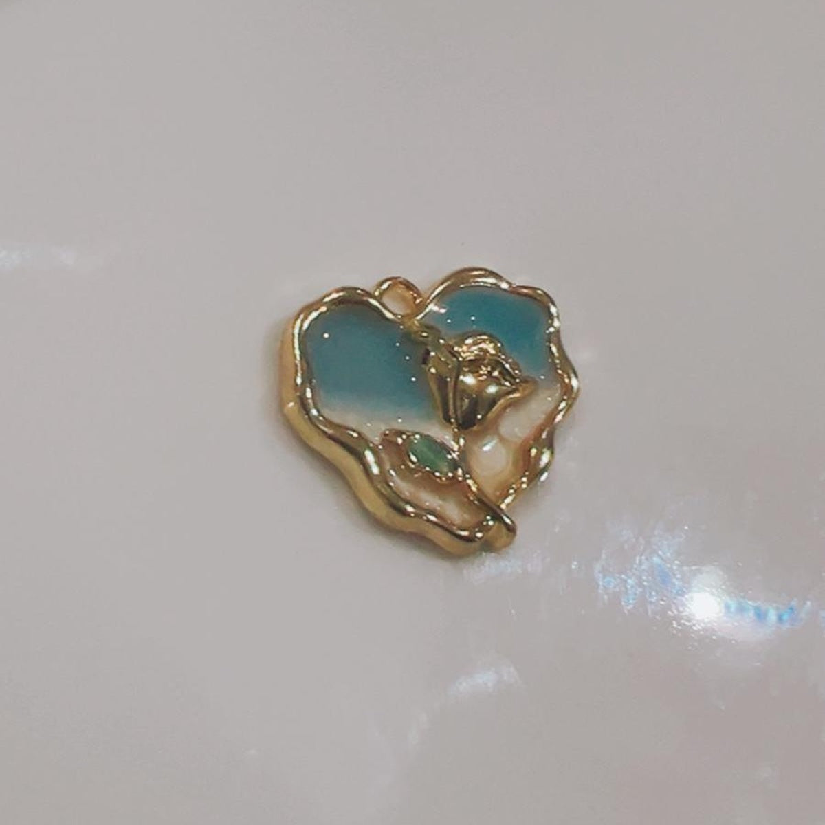 Teal and white heart charm with a rose design on a white background
