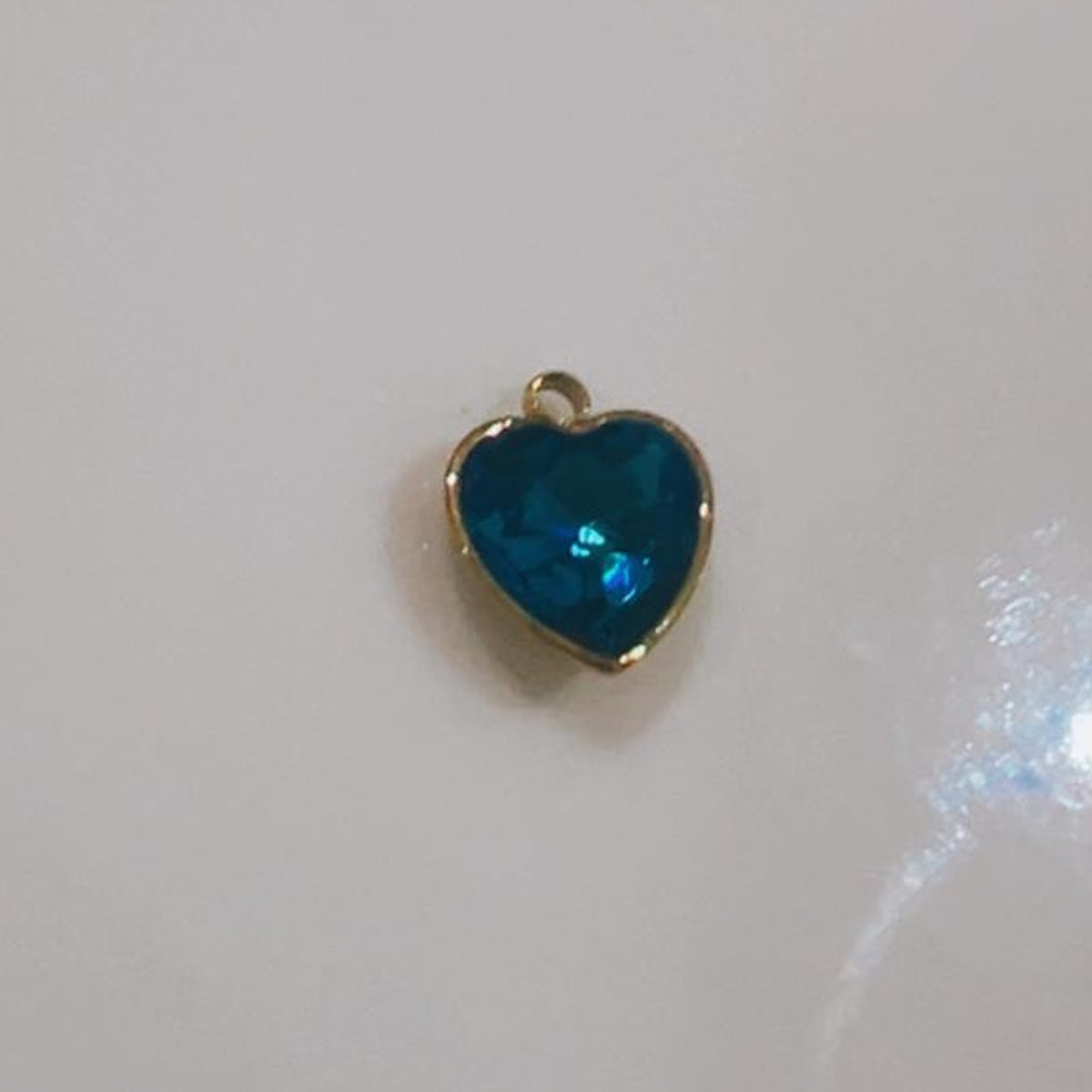 Deep teal faceted heart charm on a white background