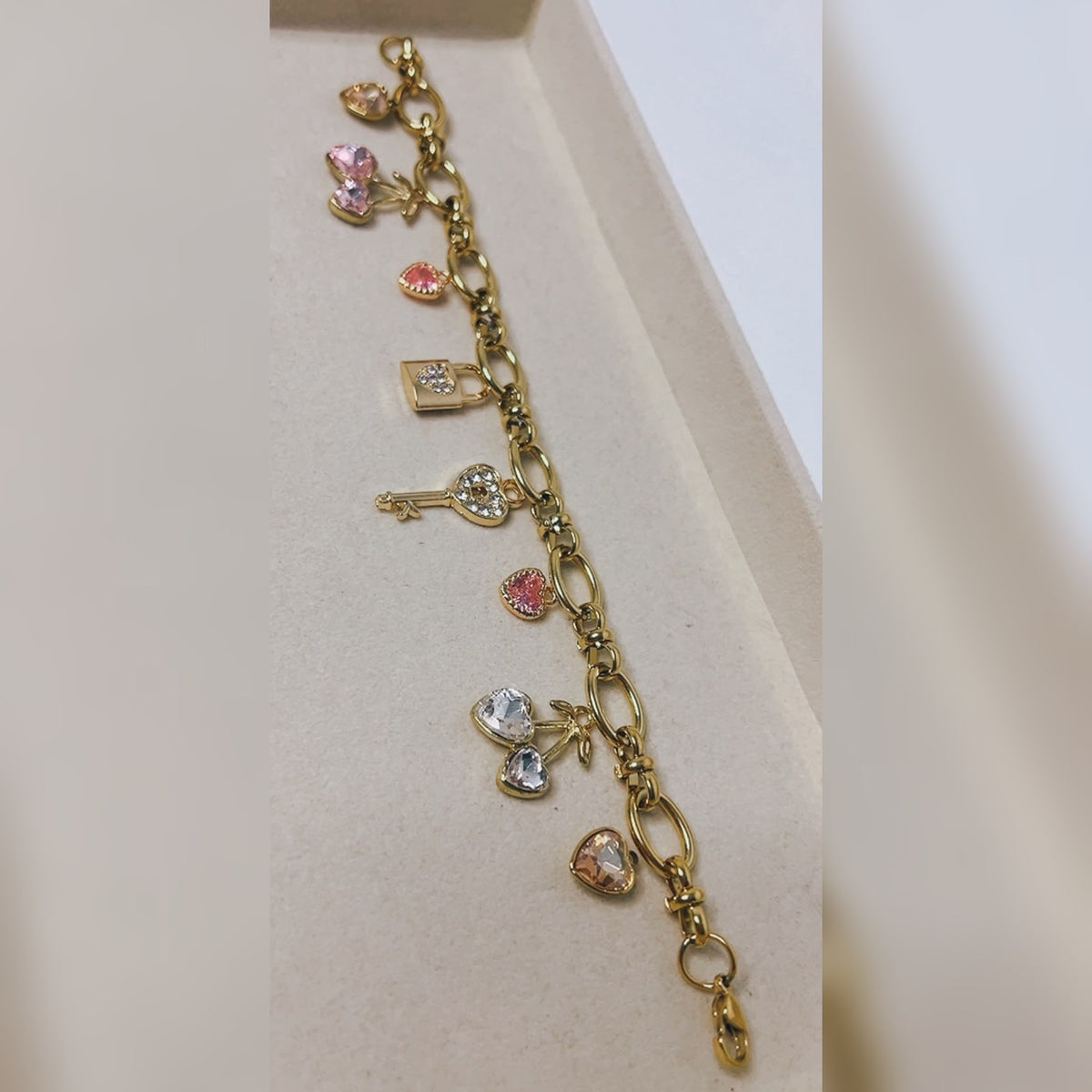 Gold charm bracelet with pink, peach and clear crystal heart charms, cherry hearts, a lock and a key
