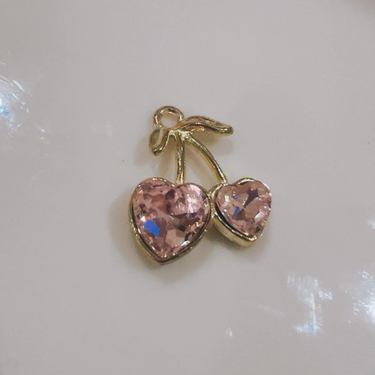 Pink cherry hearts charm with two pink hearts and a green leaf on a white background