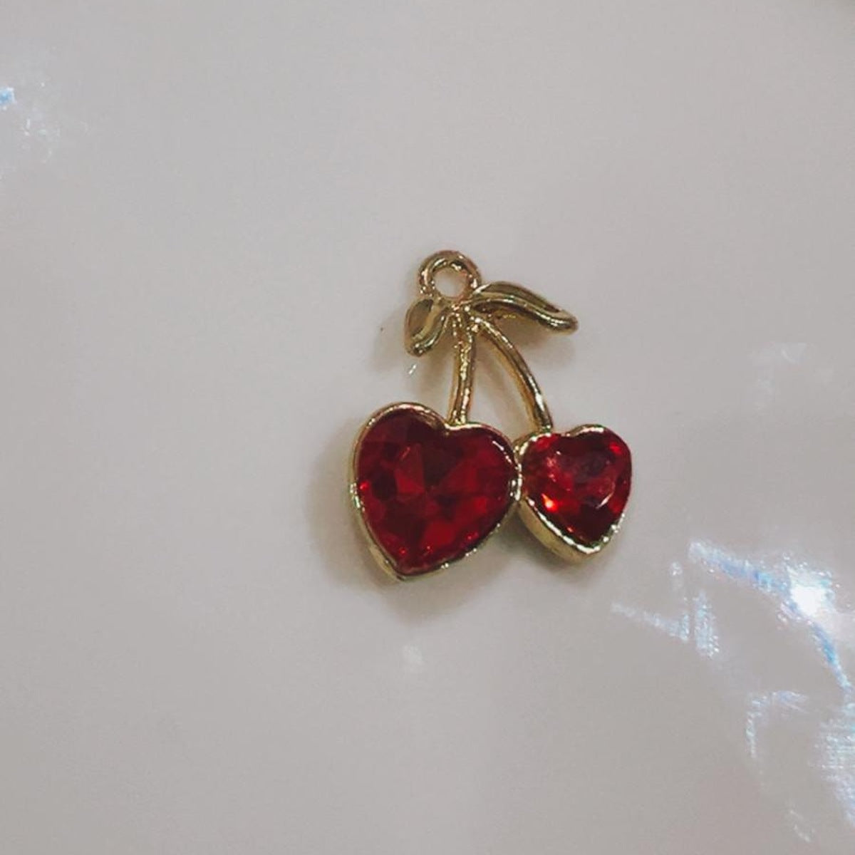Red cherry hearts charm with two red hearts and a green leaf on a white background