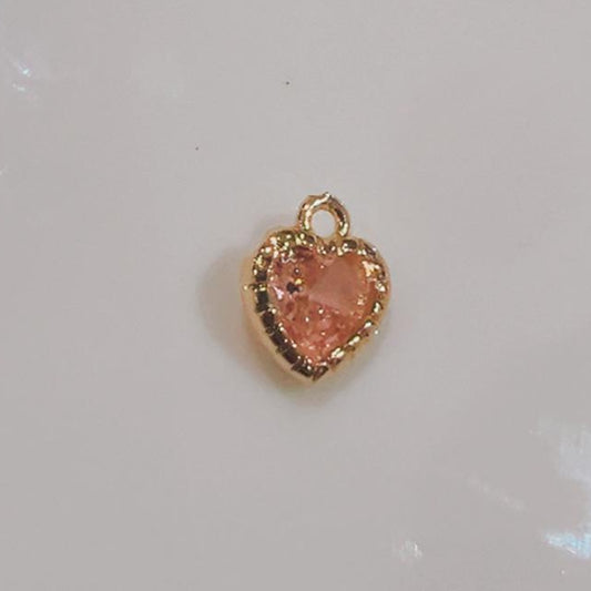 Small peach pink heart charm with a beaded edge on a white background