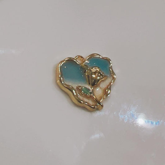 Teal and white heart charm with a rose design on a white background
